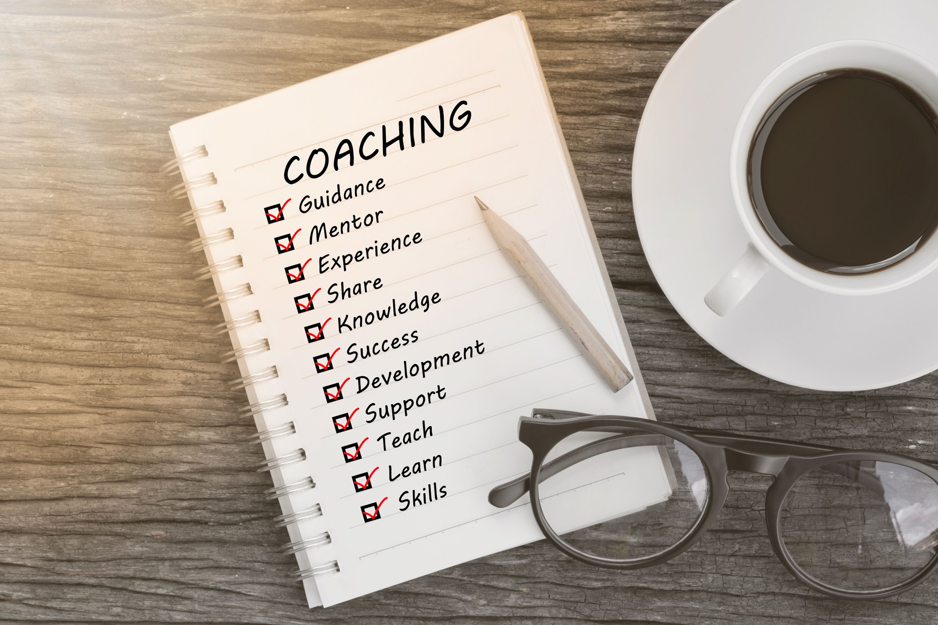 coaching and check list marks in notebook with glasses, pencil and coffee cup on wooden table. Project management concept.